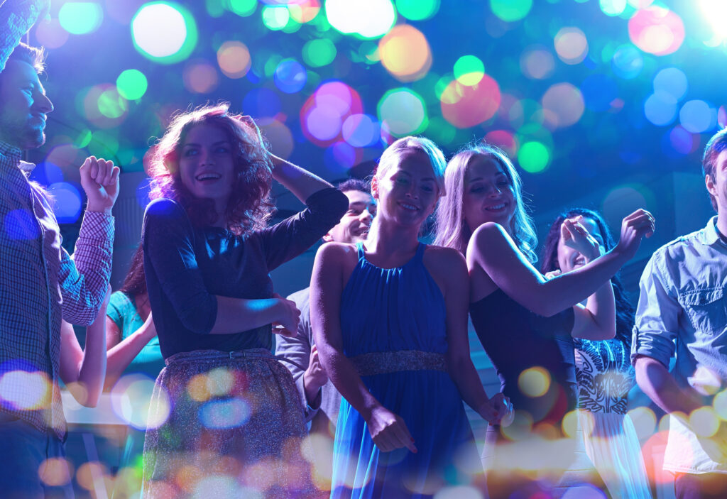 group of happy friends dancing in night club